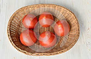 Five red large tomatoes lie in a wicker basket
