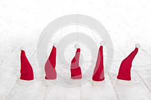 Five red santa hats on snowy white wooden background for Christm photo