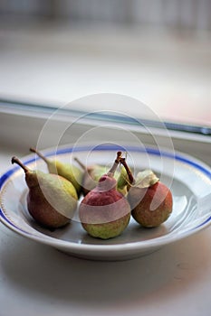 Five ripe pears in a plate on the windowsill