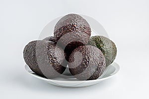 Five ripe ready to eat avocado fruits on a white plate on a white table, with side view