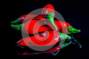 Five red chili peppers isolated on a black reflecting background