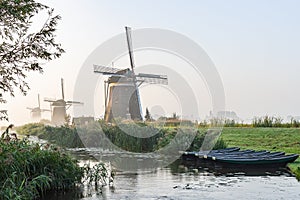 Five rowing boats in the ditch at the three wind mills of Molendriegang Leidschendam, Netherlands during a misty Sunrise