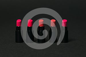 Five samples of red lipstick on a black background.