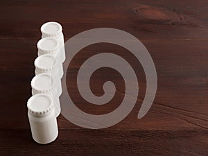 Five small plastic white banks with lids on a wooden background