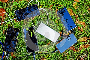 five smartphones charging from an outlet on the grass, flatlay. Family trip in nature,