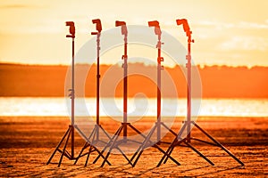 Five speedlights stand on lightstands on the beach in the sunset