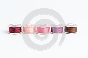 Five spools of burgundy, light pink, pink, mauve and brown threads prepared for the sewing machine, isolated on white, side view