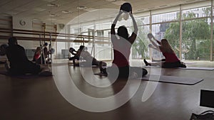 Five sportive people sitting on sport mat and bending holding ball in hands. Back view of Caucasian men and women