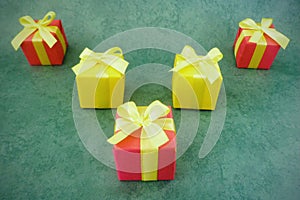 Five square red and yellow gift boxes on green textured background, red one at the front .