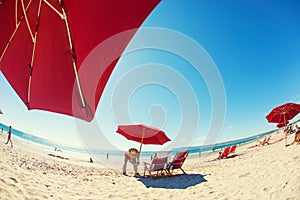 A five-star service: A beach assistant assembling red sun umbrella near lounge chairs.