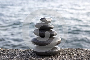 Five stones cairn tower, rock zen sculpture, black pebbles and ocean light blue background