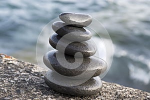 Five stones cairn tower, rock zen sculpture, black pebbles and ocean light blue background