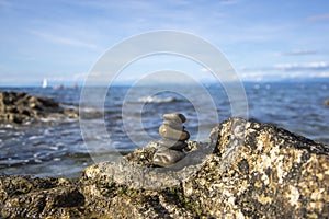 Five stones cairn tower, rock zen sculpture, brown beige pebbles on the rock and sea light blue background