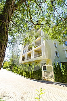Five-story residential building with a fence of cypress trees and an elegant white gate