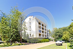 Five-story residential building with a fence of cypress trees and an elegant white gate