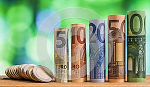 Five, ten, twenty, fifty and one hundred euro rolled bills banknotes, with euro coins on green blurred bokeh background.