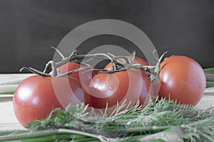 Five tomatoes with herbs on a black background close up.