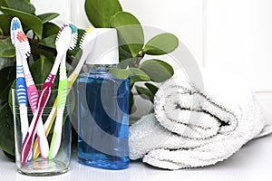 Five toothbrushes in a glass cup mouthwash and a rolled up towel on the dressing table against the green foliage