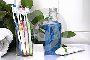 Five toothbrushes in a glass cup mouthwash a tube of toothpaste and a rolled up towel on the dressing table against a backdrop of