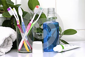 Five toothbrushes in a glass cup mouthwash a tube of toothpaste and a rolled up towel on the dressing table against a backdrop of