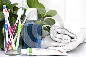 Five toothbrushes in a glass cup mouthwash a tube of toothpaste and a rolled up towel on the dressing table against a backdrop of