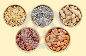 Five types of snacks in brown bowl: sunflower seeds, pumpkin seeds, peanuts, raisins, almonds. Above shot. Different samples