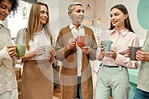 Five well-dressed women of different age having a morning coffee break during a brainstorm