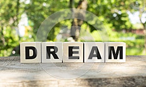 Five wooden blocks lie on a wooden table against the backdrop of a summer garden and create the word DREAM.