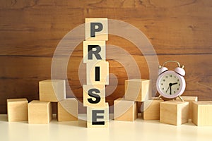 Five wooden cubes stacked vertically on a brown background make up the word PRISE. photo