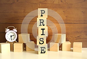 Five wooden cubes stacked vertically to form the word PRISE on a brown background. photo