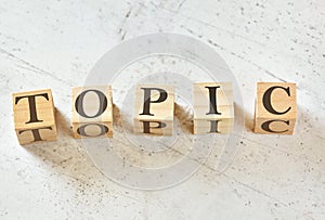 Five wooden cubes with word TOPIC on white stone like board, view from above