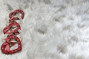 Five wooden heart shaped xmas ornaments on white fluffy fabric, close up