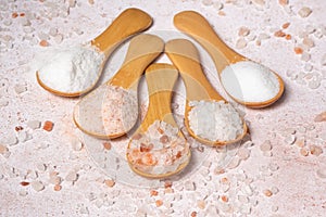Five wooden spoons with different types of salt are spread out in a fan on the table