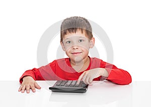 The five-year boy sitting at a white table and presses the button calculator