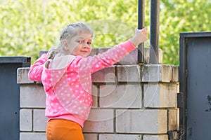 Five-year girl climbed on brick fence and turned around looked at the frame