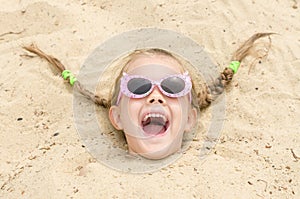 Five-year girl with glasses on a beach strewn on his head in the sand