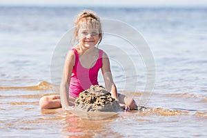 Five-year girl in a pink bathing suit playing in sand in the shallows of the river