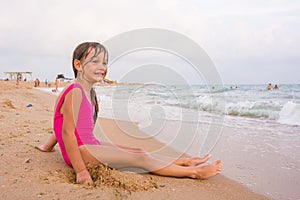 Five-year girl sits on beach and seaside fun looking into the distance