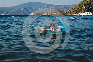 Five-year-old boy in a blue lifebuoy learns to swim in the sea, Turkey