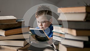 Five year old boy in glasses reading a book with a stack of books next to him. Smart intelligent preschool kid choosing books to