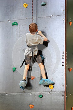 Five year old boy learning to climb the rock wall outside in the summer park.