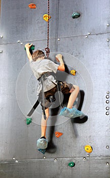 Five year old boy learning to climb the rock wall outside in the summer park.