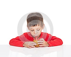 The five-year-old boy sits at a white table and drinking orange juice