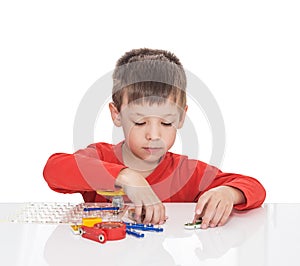 The five-year-old boy sits at a white table and plays an electronic designer