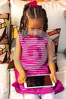Five-year-old Colombian Afro-descendant Latina girl sitting on the sofa next to the Christmas tree checking her tablet
