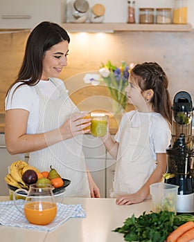 Five year old daughter with her mom drinks homemade beverage which was made in juicer. Vegan drinks