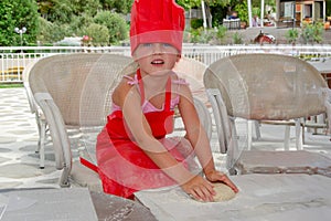 five-year-old girl in chef\'s hat kneads dough