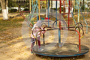 A five-year-old girl tries to unwind on the carousel turntable in the fall. Playground.