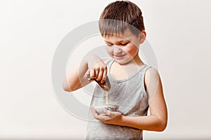 Five-year-old smiling Russian boy smears a rolled butter pancake into liquid honey on a white background. Russian Maslenitsa
