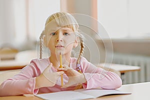 Five years old blonde girl sitting at classroom and writing